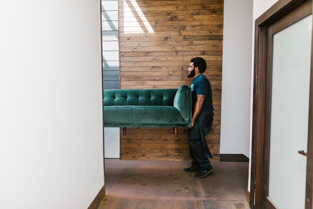 Person carrying a couch in a hallway